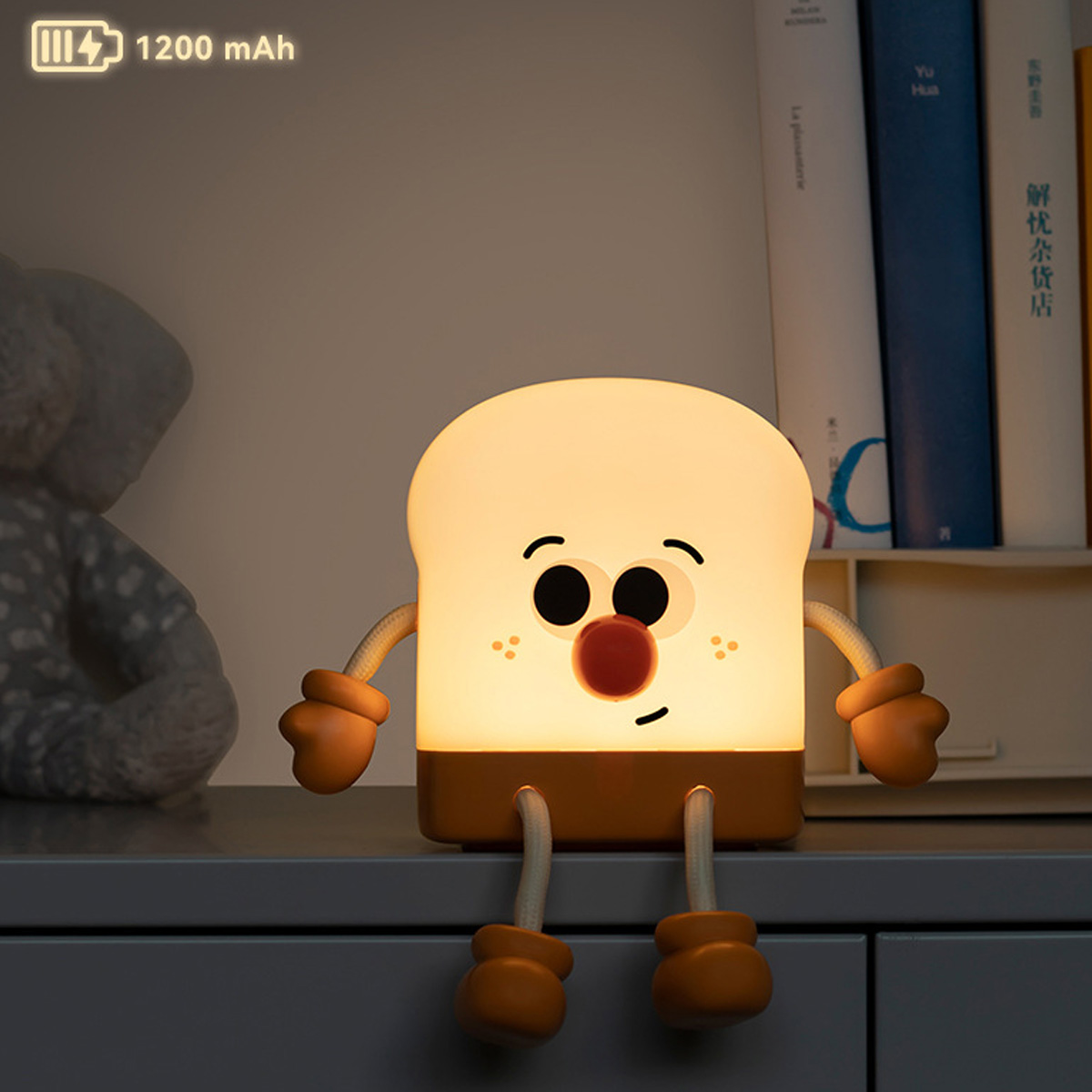 Eine toastbrotförmige LED-Lampe mit Gesicht sitzt auf einem Regal, mit gedrucktem Text "1200 mAh" oben links.