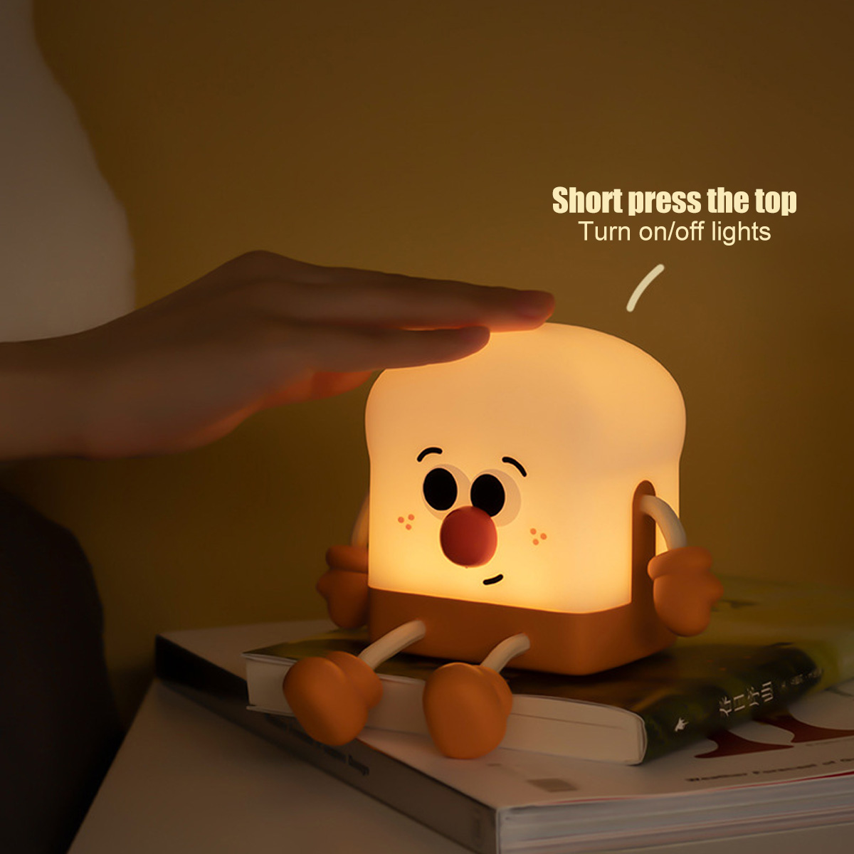 Eine Hand berührt eine kleine, leuchtende Toastbrot-Lampe mit Gesicht, die auf Büchern sitzt.