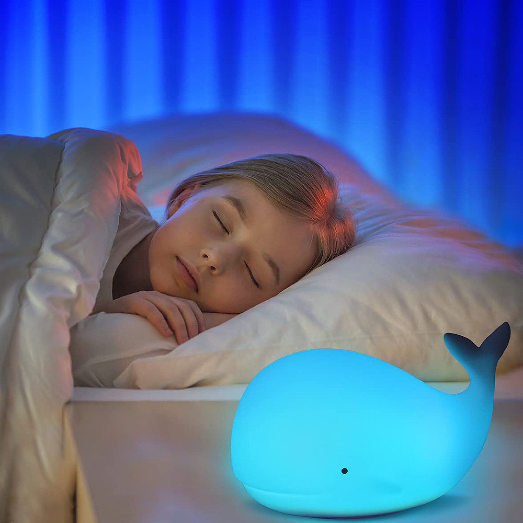 Ein Kind schläft friedlich im Bett neben einer leuchtenden blauen Wal-Lampe.