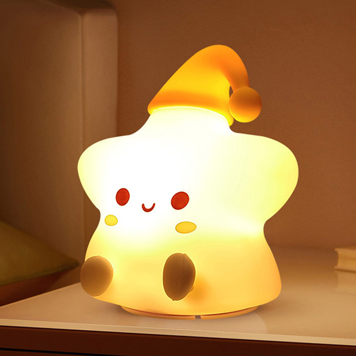 Eine niedliche sternförmige Nachtlampe mit gelber Mütze leuchtet warm auf einem Nachttisch.