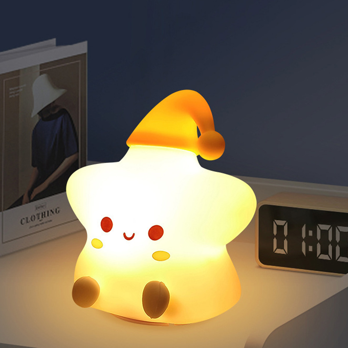 Ein leuchtendes Sternen-Nachtlicht mit Schlafmütze, ein Buch und ein Digitalwecker auf dem Nachttisch.