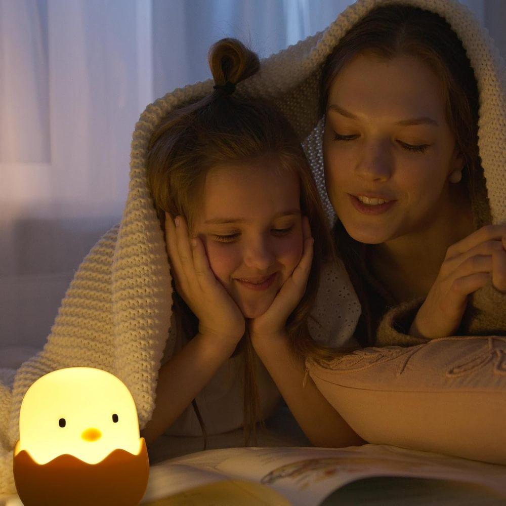 Eine Mutter und Tochter lesen ein Buch unter einer Decke, beleuchtet von einer gelben Kükenlampe.