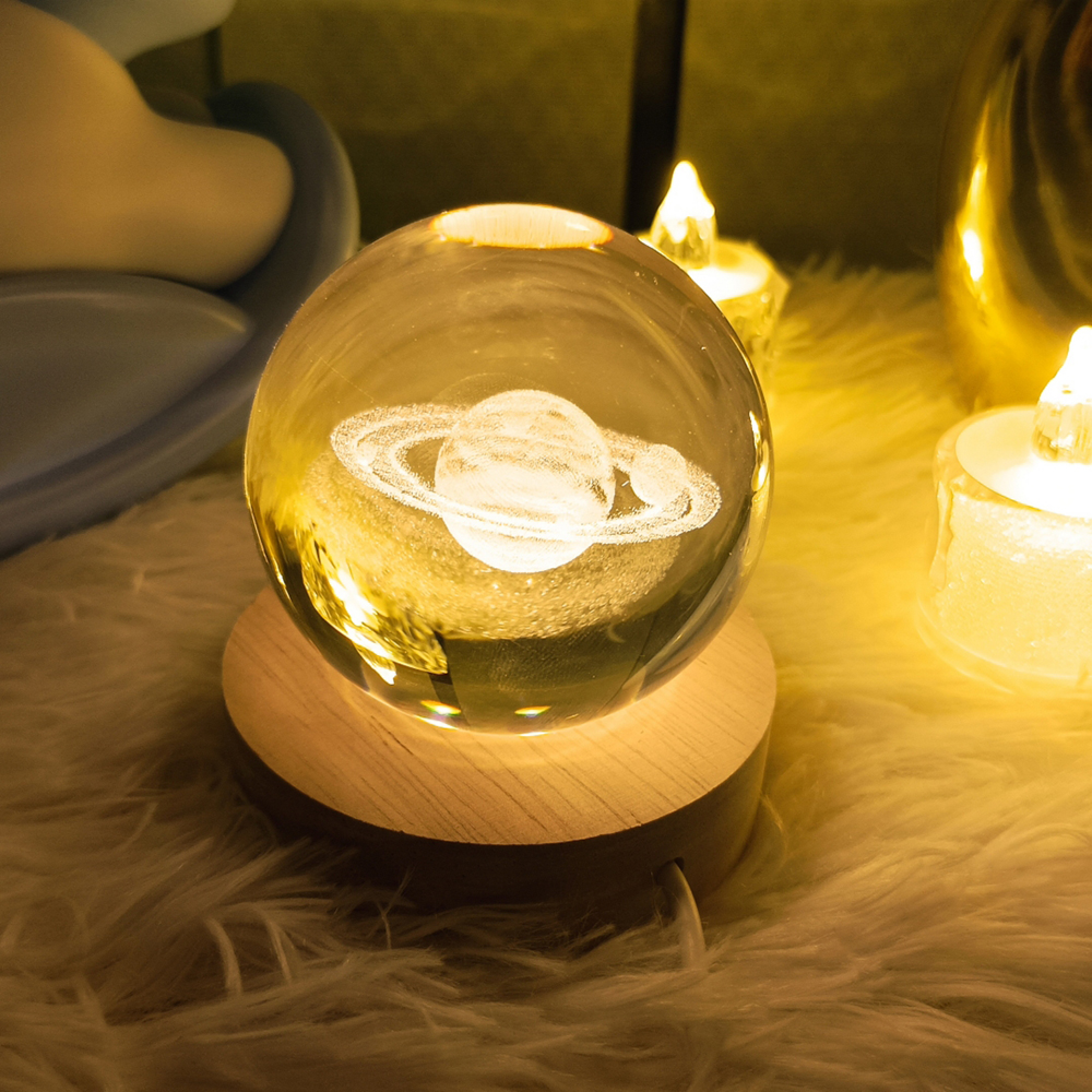 Eine Glaskugel mit Saturn-Gravur sitzt auf einem beleuchteten Holzsockel, umgeben von Kerzen.