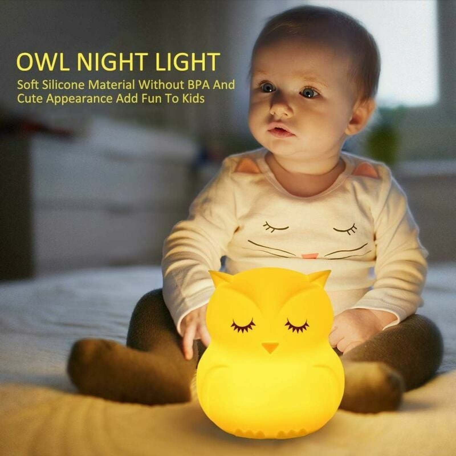 Ein Baby sitzt auf dem Bett mit einer leuchtend gelben Eulen-Nachtlampe.