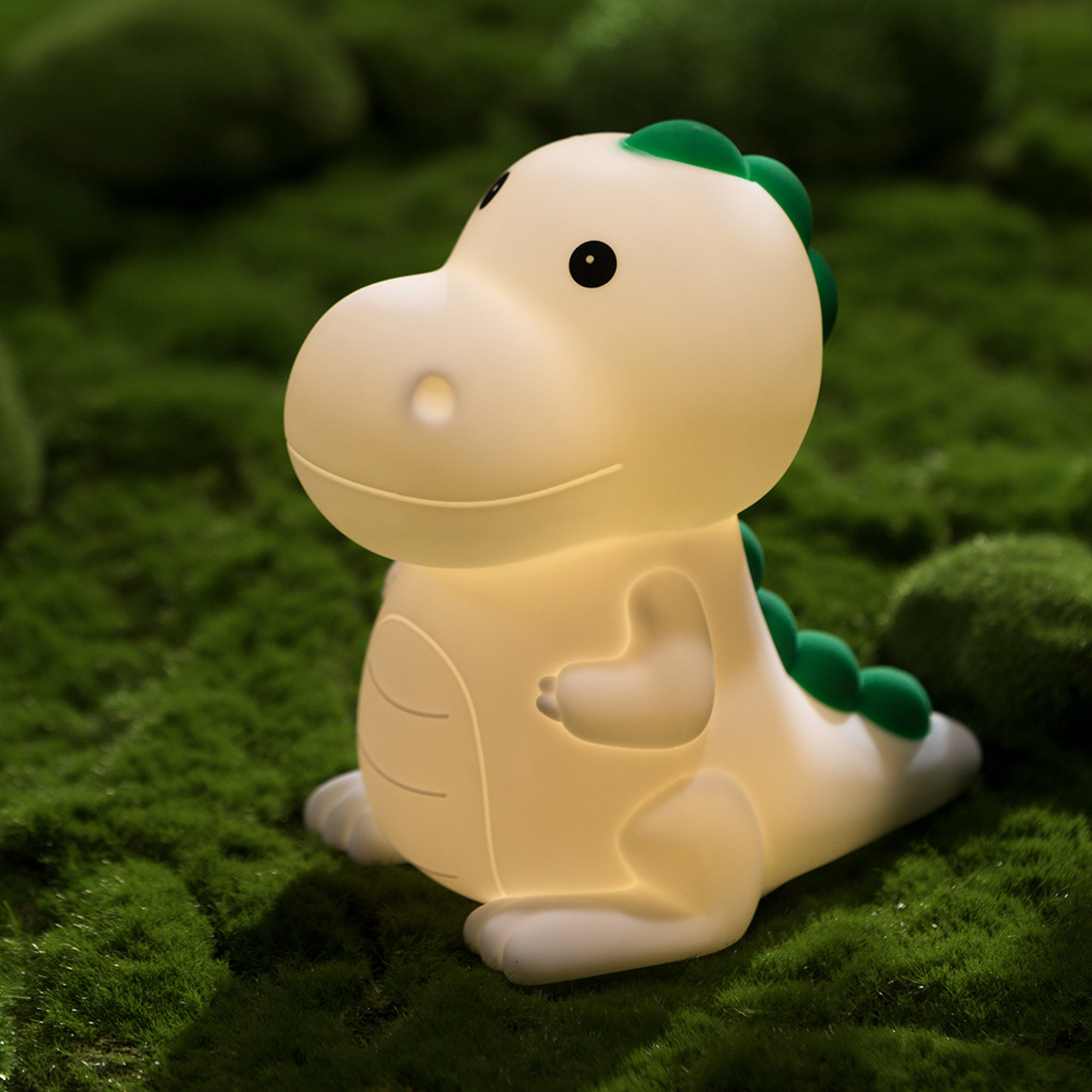 Eine kleine weiße Dinosaurier-Nachtlampe mit grünen Stacheln sitzt auf weichem grünem Moos.