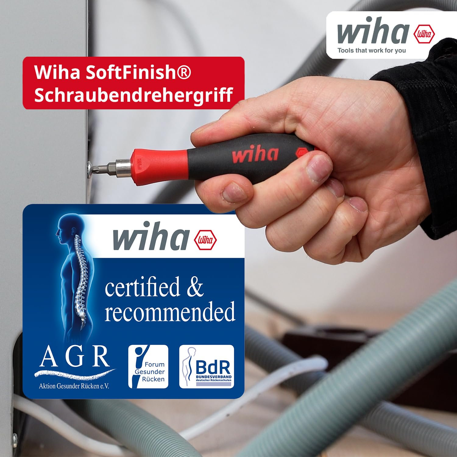 Una mano tiene un cacciavite Wiha SoftFinish rosso e nero mentre avvita un elettrodomestico.