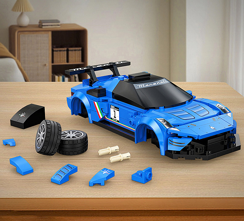 Ein unvollständiges blaues Lego Maserati Rennauto auf einem Holztisch, umgeben von Steinen, Reifen und Stiften.