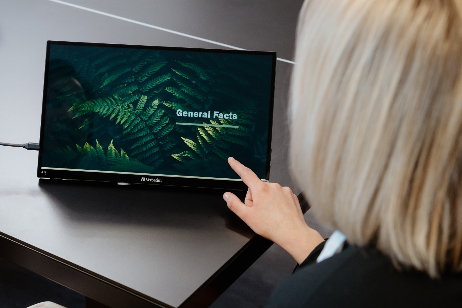 Una donna bionda tocca un monitor portatile che mostra General Facts.