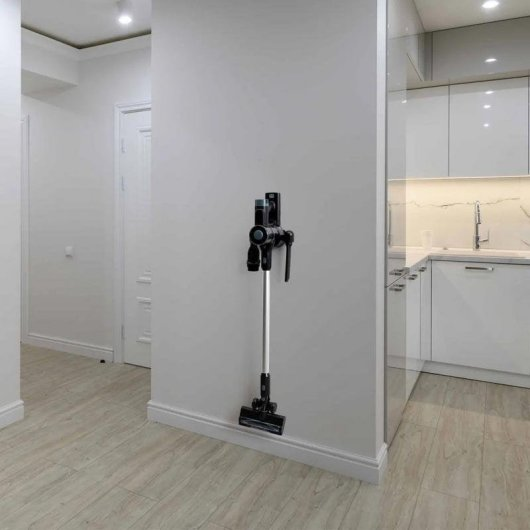 Una aspiradora inalámbrica cuelga de una pared en un apartamento blanco y moderno cerca de la cocina.