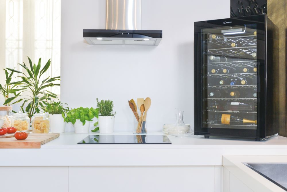 Una moderna cucina bianca con cantinetta nera, piante, utensili da cucina e piano cottura con cappa.