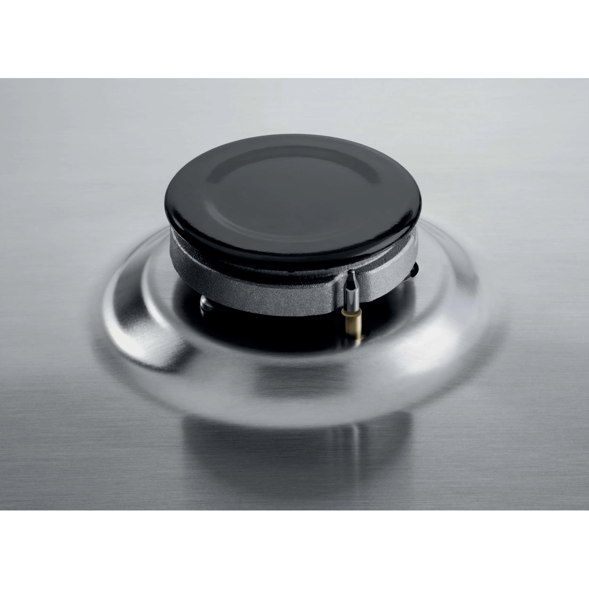 A shiny, round gas burner on a silver stainless steel surface with a small metal ignition pin.