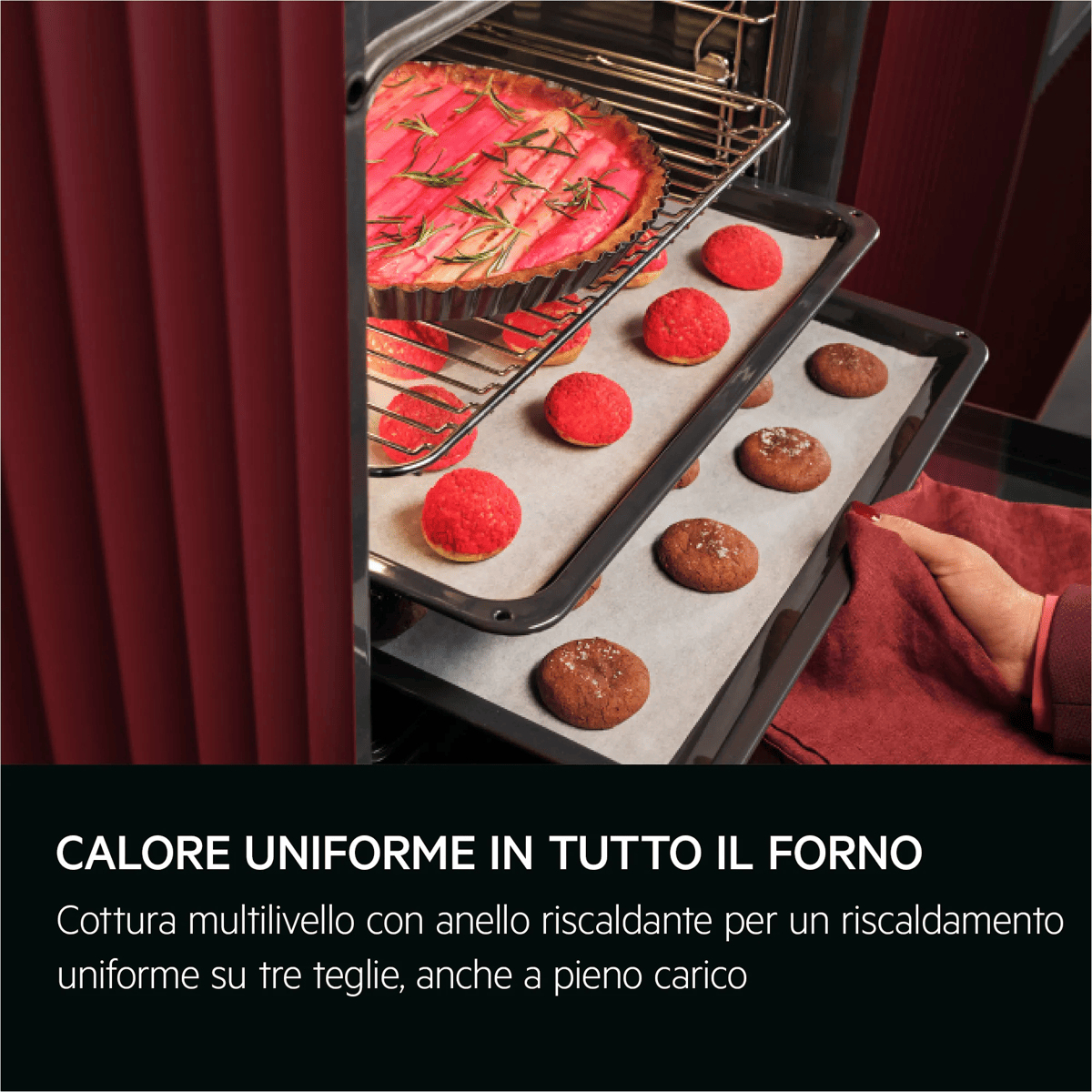 Un forno rosso aperto con tre teglie piene di prodotti da forno, tra cui una crostata e biscotti.