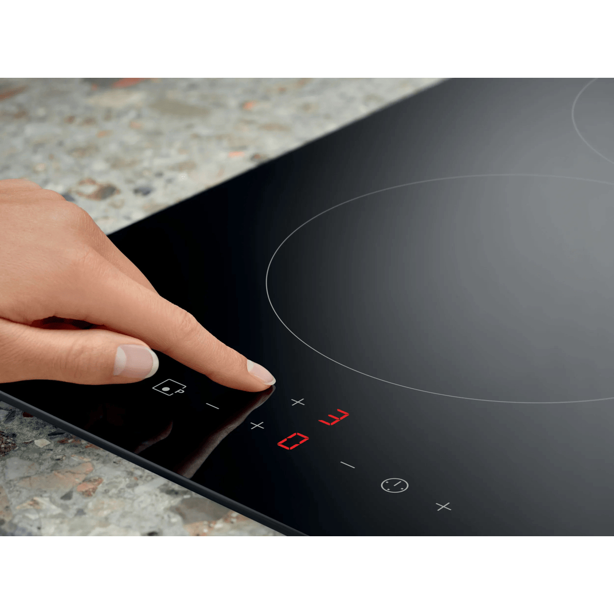 A hand operates the touch controls on a black induction cooktop with red LED indicators.