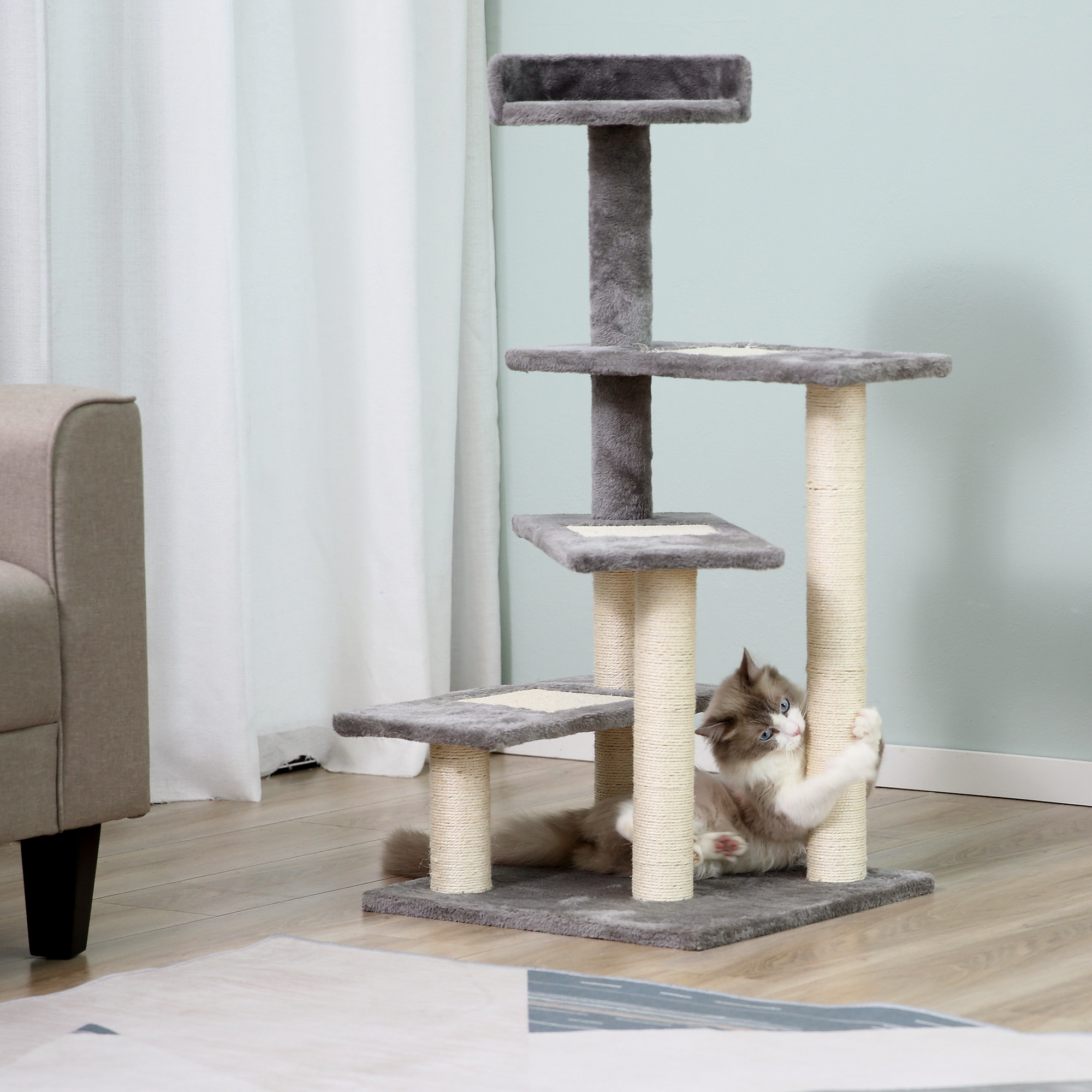 Un gatto soffice graffia un palo in sisal su un tiragraffi grigio a più livelli in una stanza luminosa.