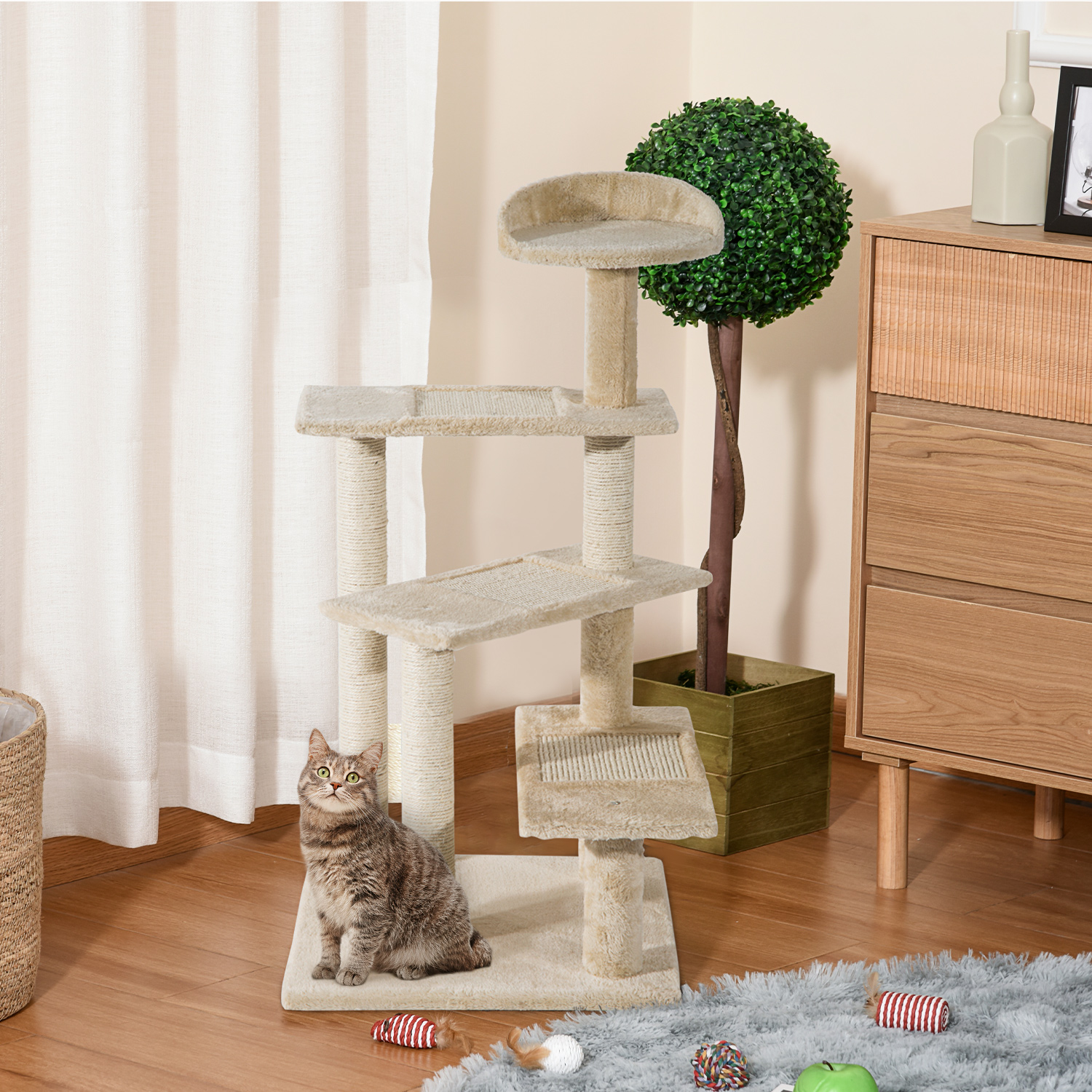 Un gatto tabby siede accanto a un tiragraffi beige su pavimento in legno vicino a tenda e comò.