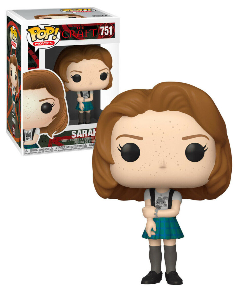 Sarah Vinyl-Figur aus The Craft mit braunen Haaren, Sommersprossen, Karo-Rock, neben der Verpackung.