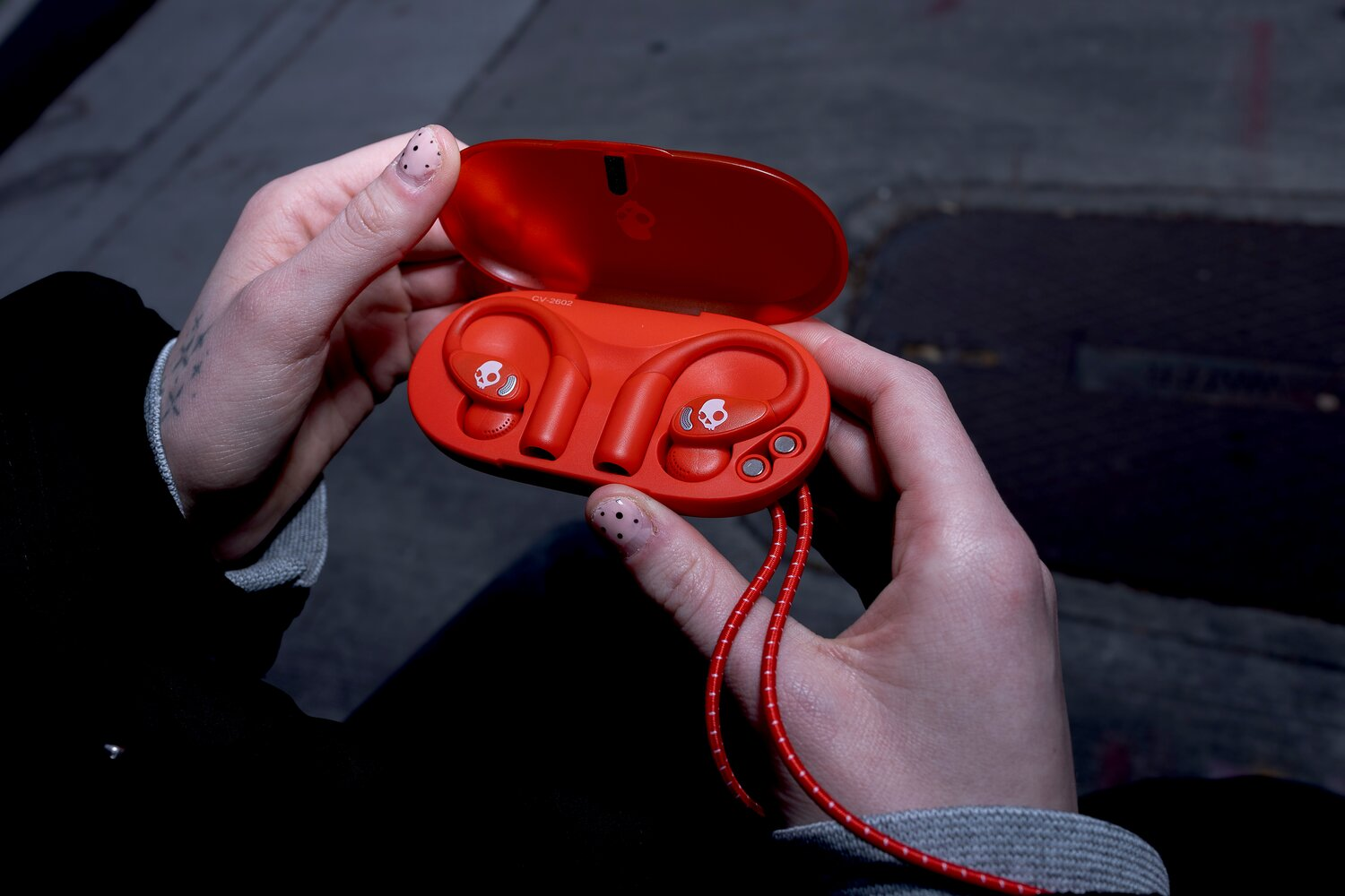 Persona sosteniendo un estuche de carga rojo abierto con auriculares inalámbricos.