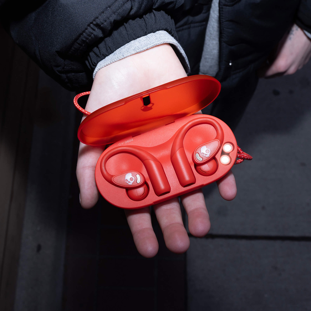 Una persona sostiene un estuche de carga rojo abierto que contiene auriculares inalámbricos.