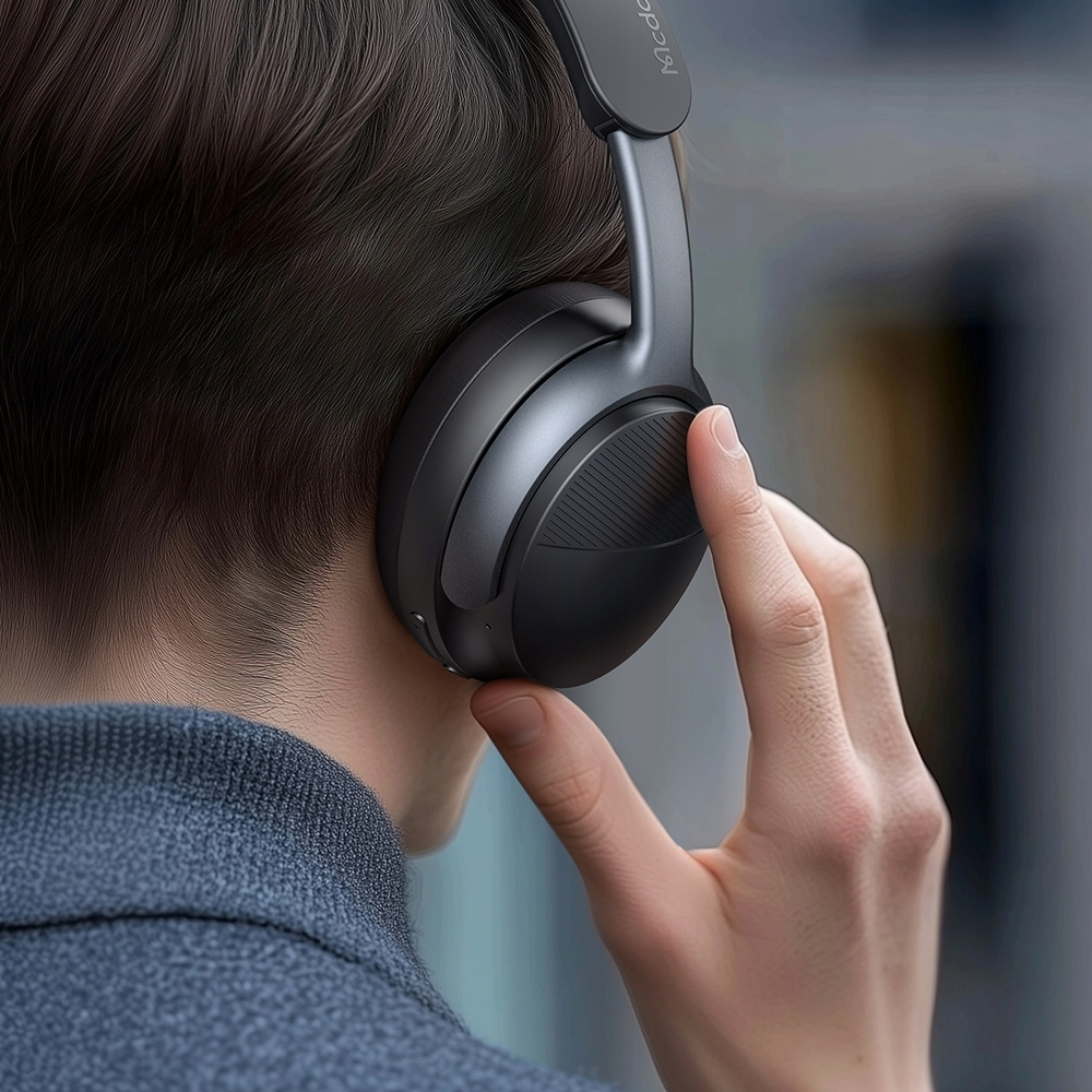 Una persona che indossa cuffie over-ear grigio scuro, mentre tocca il padiglione sinistro.