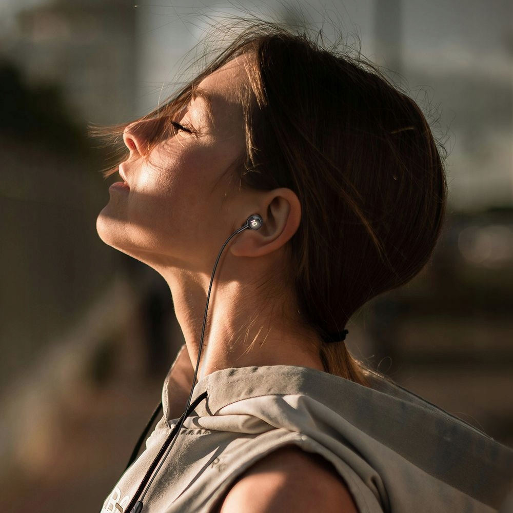 Una giovane donna con gli occhi chiusi e le cuffie si gode la luce del sole all'aperto.
