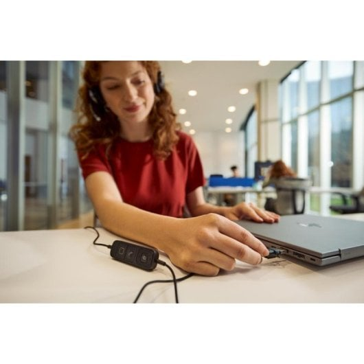Una donna con una maglietta rossa collega un cavo USB a un computer.