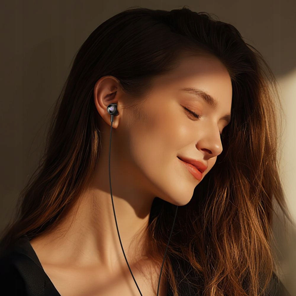 Una giovane donna con i capelli castani sorride a occhi chiusi, indossando auricolari neri.