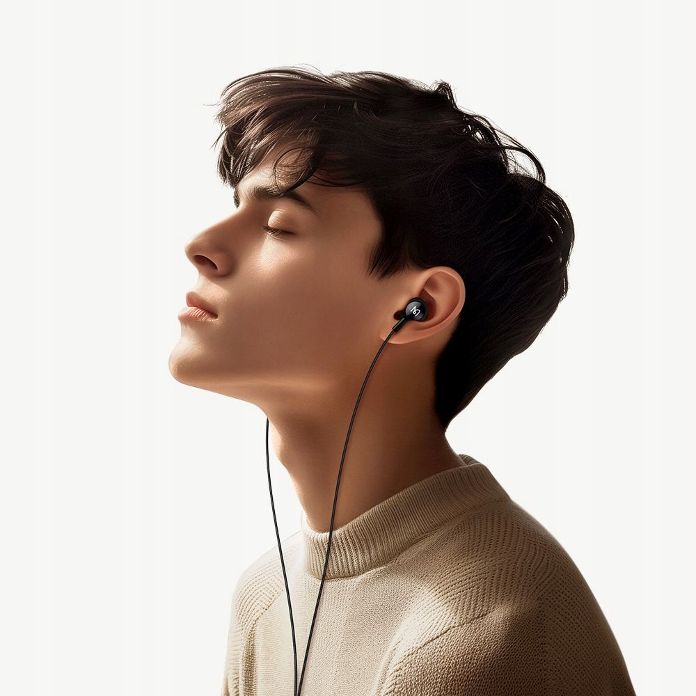 Un giovane con gli occhi chiusi indossa auricolari in-ear neri con filo e un maglione chiaro su sfondo bianco.