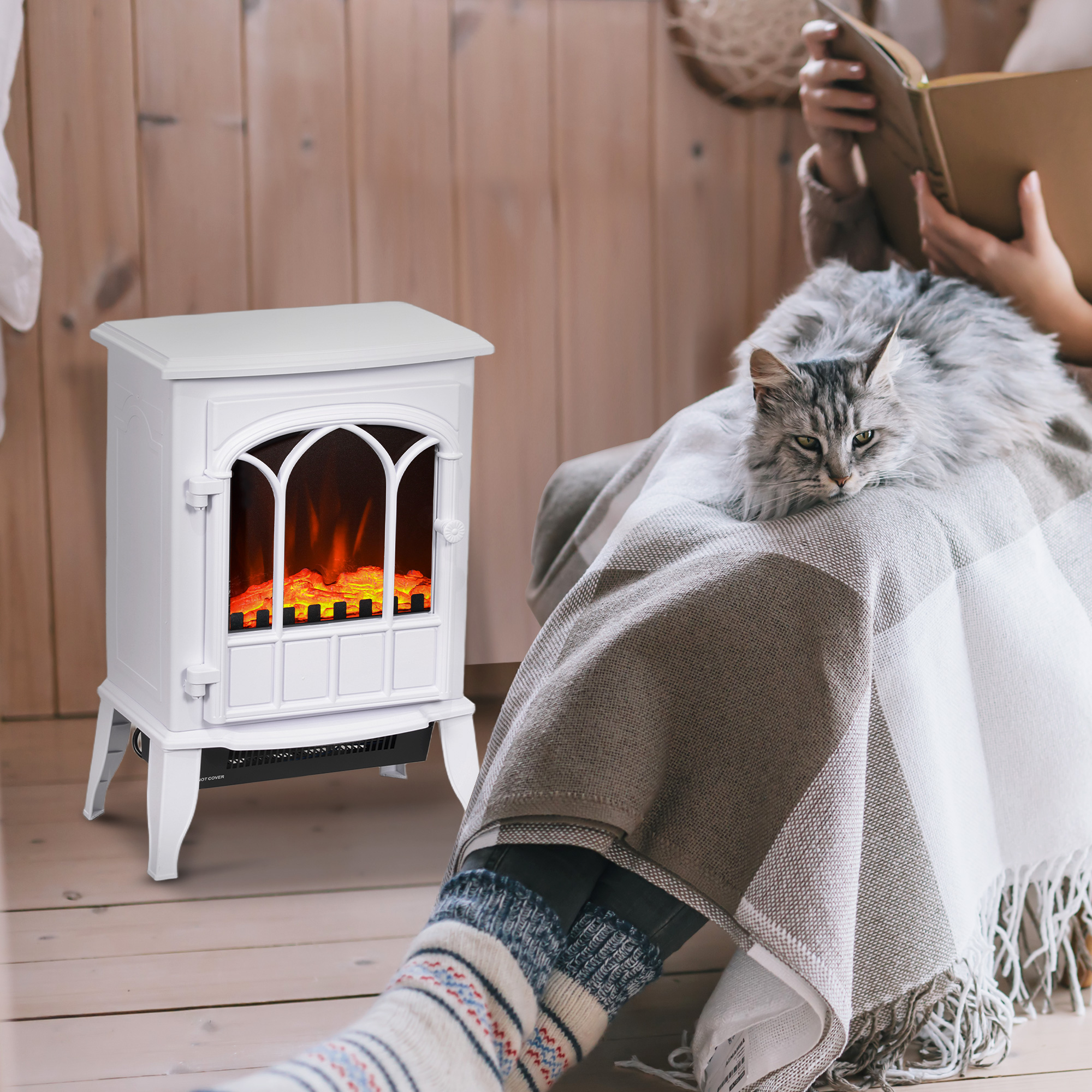 Un gato gris descansa en una manta junto a una pequeña chimenea eléctrica blanca mientras alguien lee un libro.