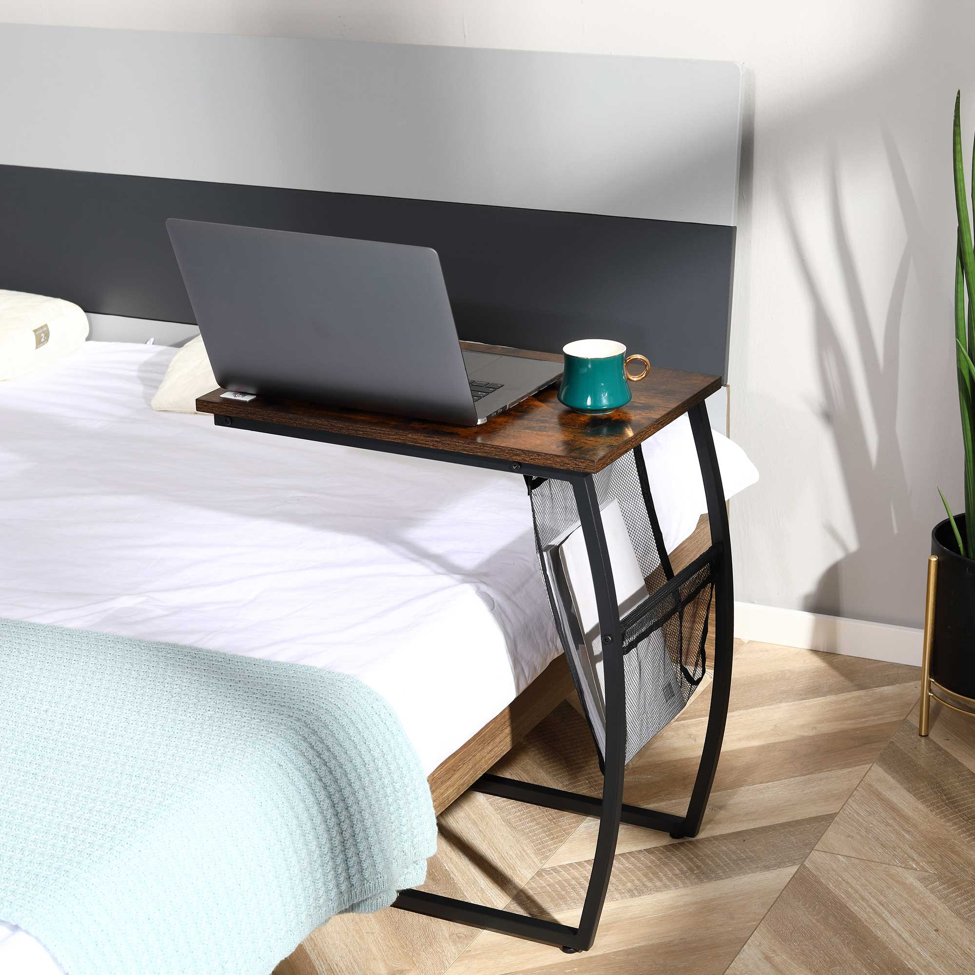 Una mesa auxiliar con una computadora portátil y una taza sobre una cama con sábanas blancas.
