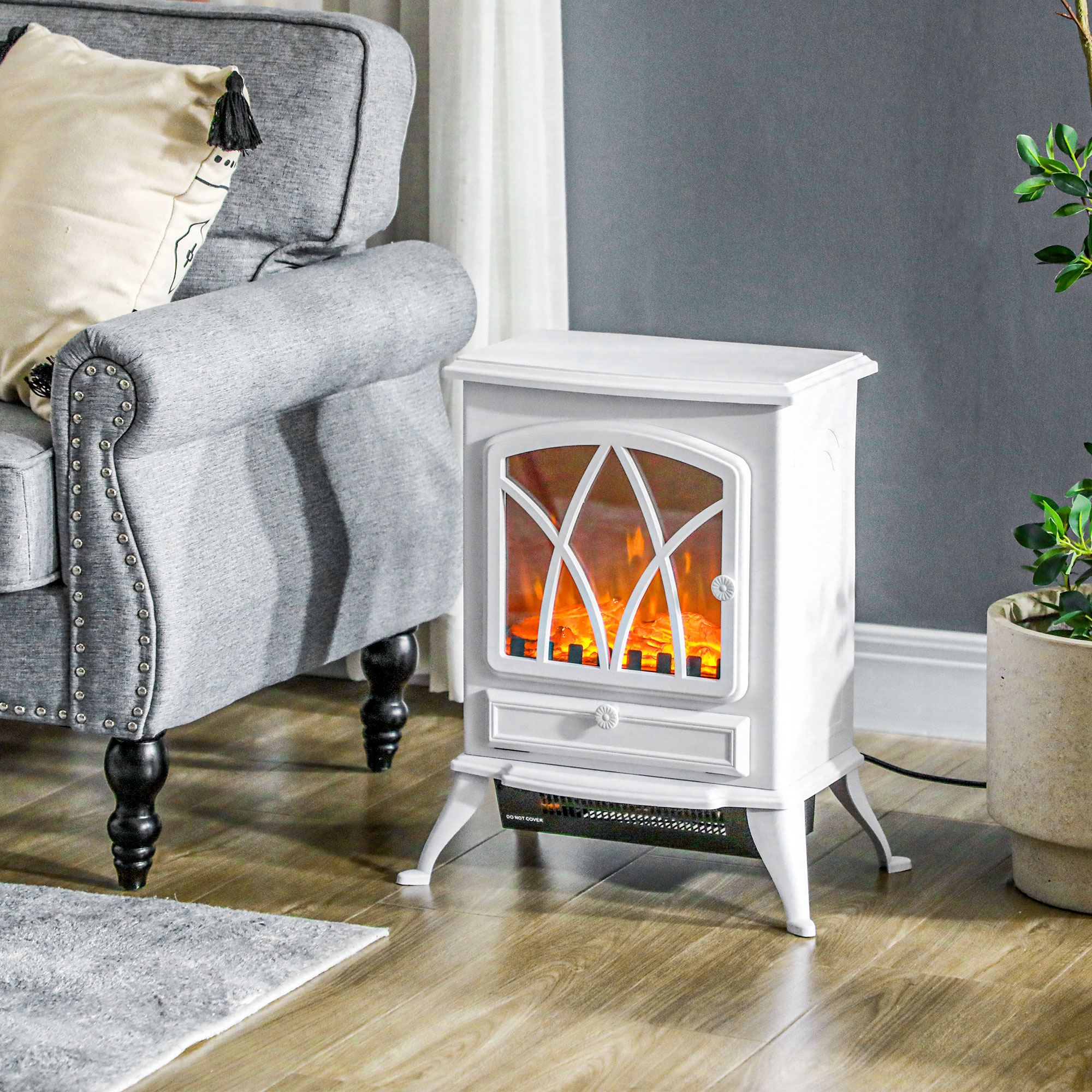 Una estufa eléctrica blanca se encuentra en el suelo de madera junto a un sillón gris y una planta.
