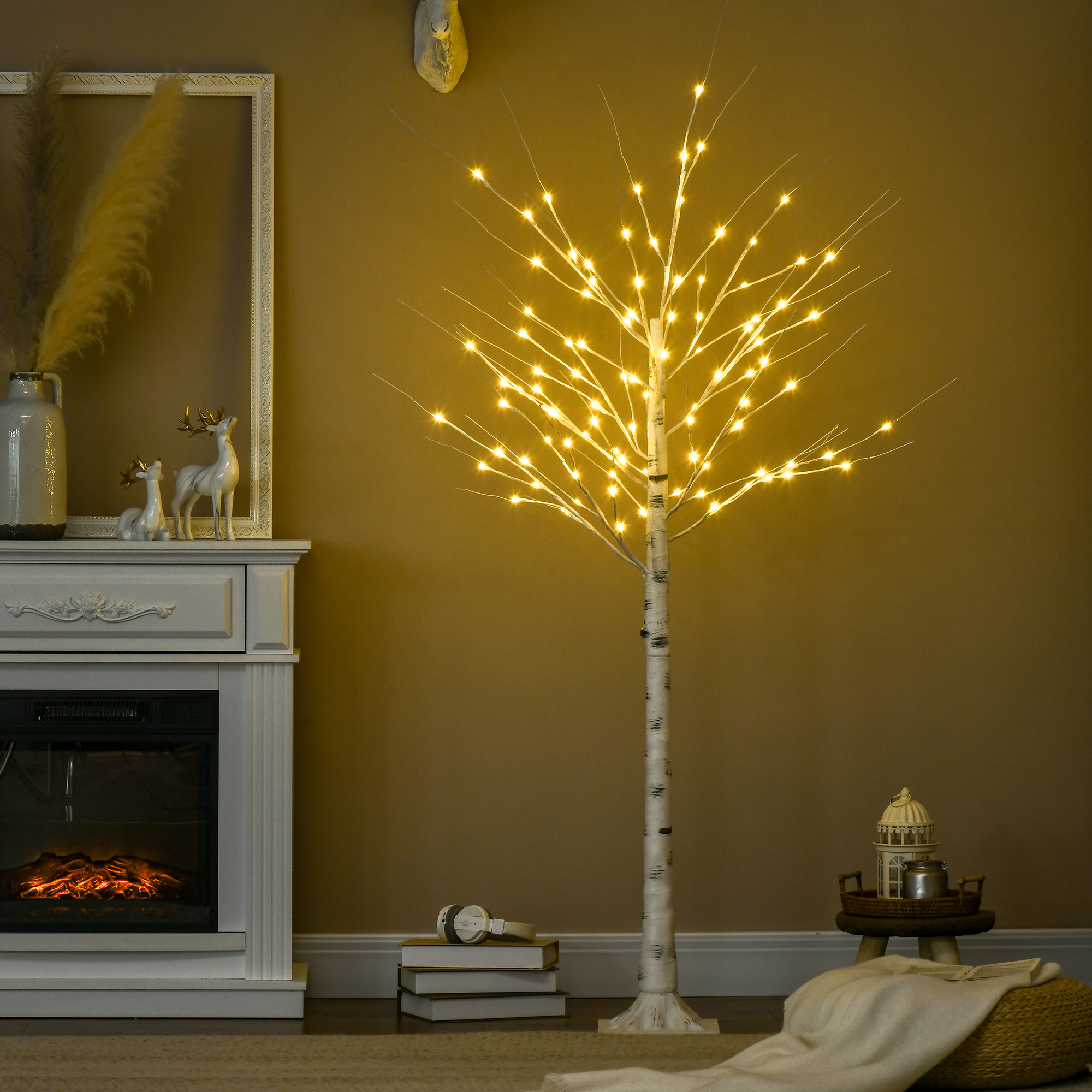 Un árbol de abedul decorativo iluminado se encuentra junto a una chimenea en una habitación cálida.