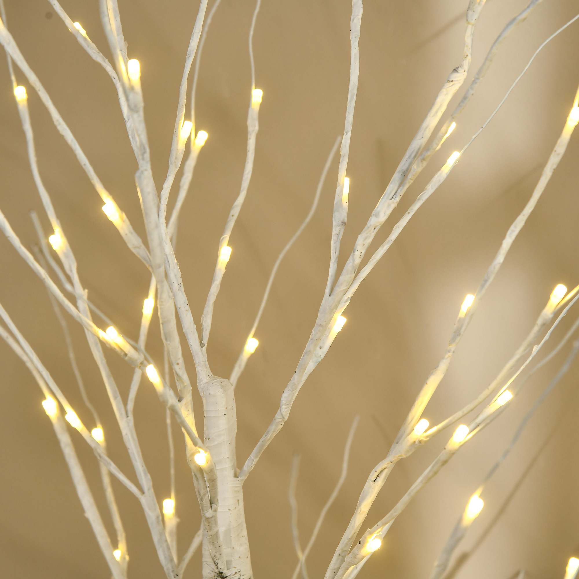 Ramas blancas de una lámpara de árbol decorativa con pequeñas luces LED cálidas sobre fondo beige.