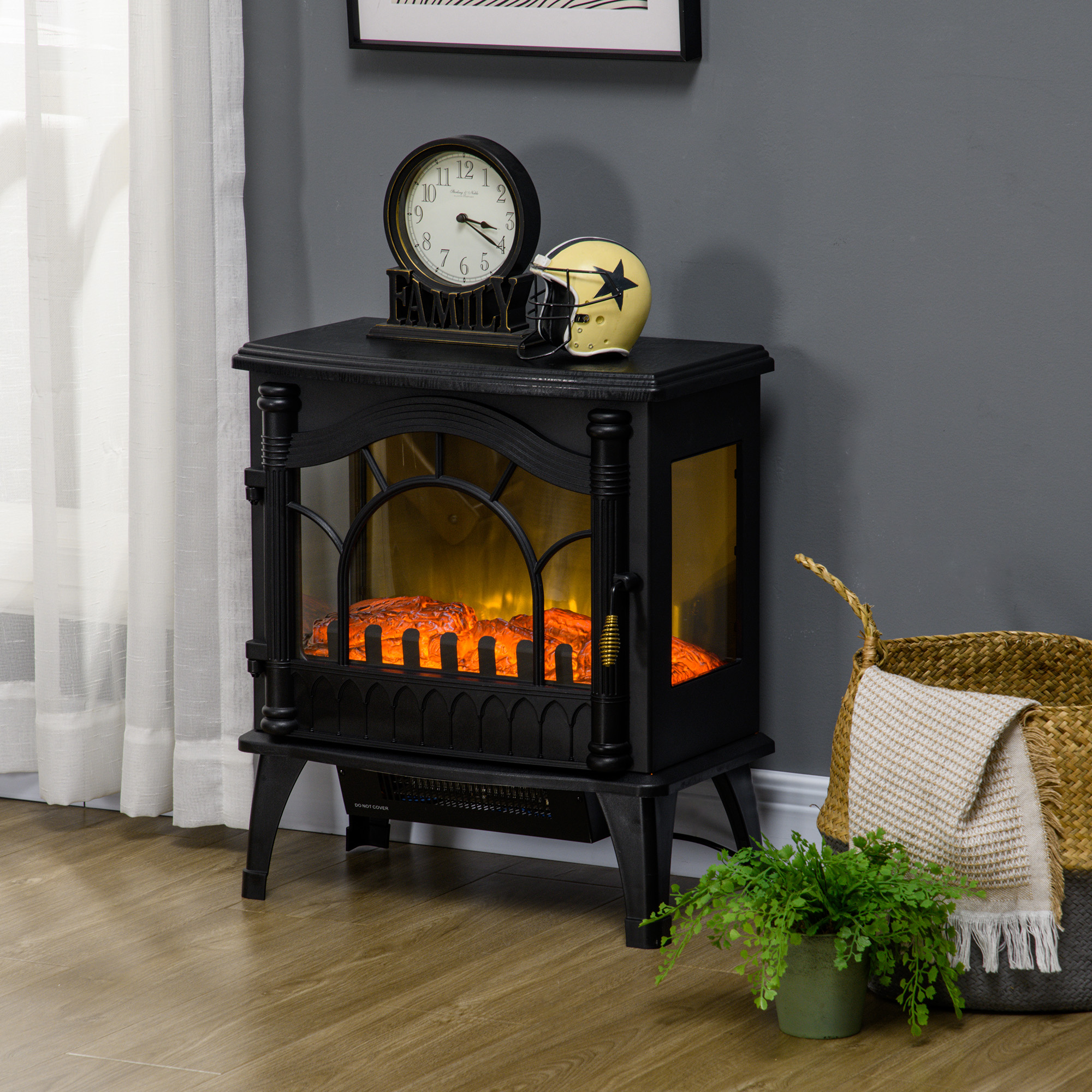 Una chimenea eléctrica negra con reloj y casco encima, al lado de una cesta tejida con manta y una planta.