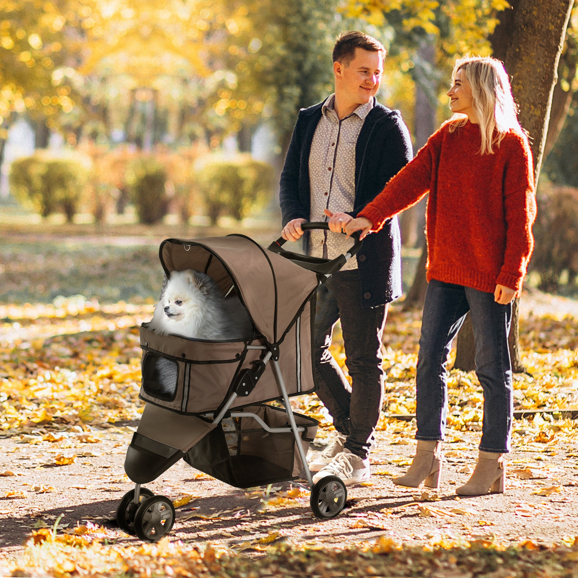 Una coppia sorridente spinge un passeggino per animali con un cane bianco in un parco autunnale.