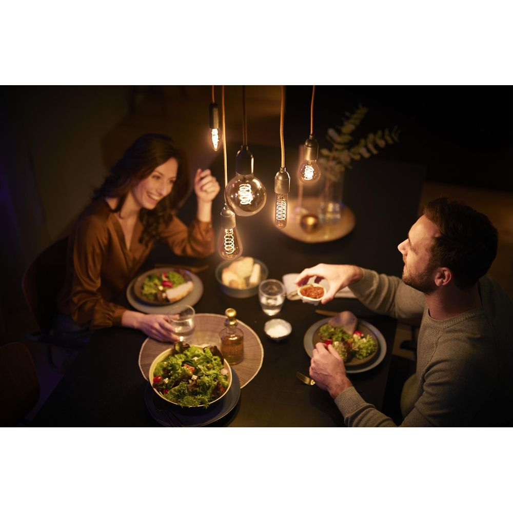 A man and a woman smiling while dining under warm hanging pendant lights at a table with salads and dishes.