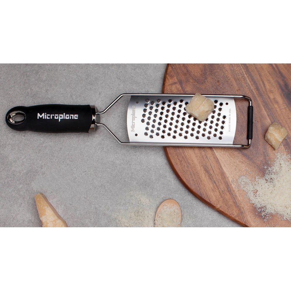 Eine Microplane-Reibe liegt auf einer Holzschneidebrett- und Steinoberfläche mit Käsestücken.