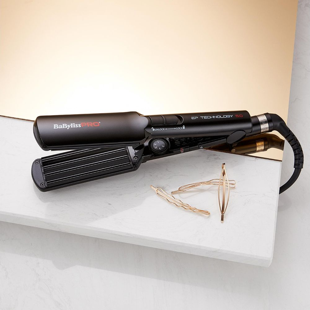 Una piastra per capelli nera BaBylissPRO su una superficie di marmo con forcine dorate.