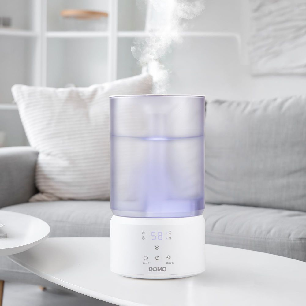 Un humidificateur blanc avec affichage numérique posé sur une table dans un salon lumineux.