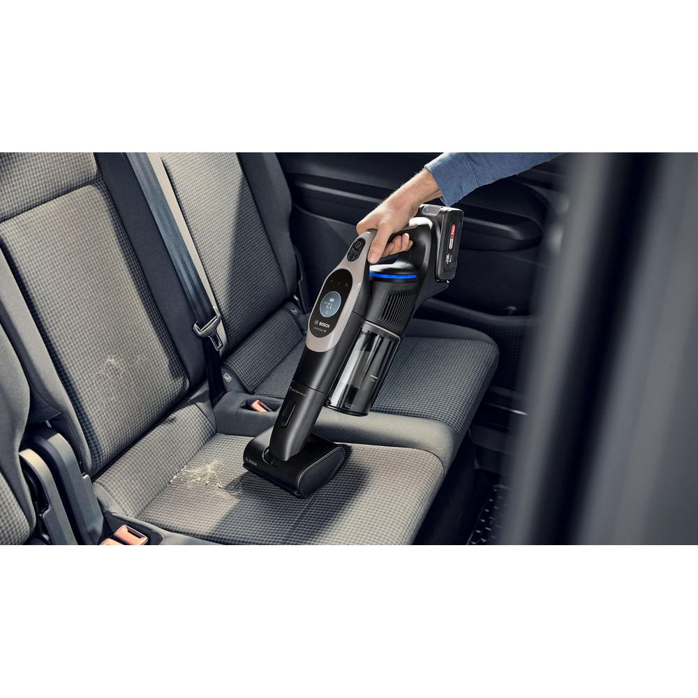 Una mano usa un aspirapolvere senza fili nero per pulire un sedile d'auto grigio.