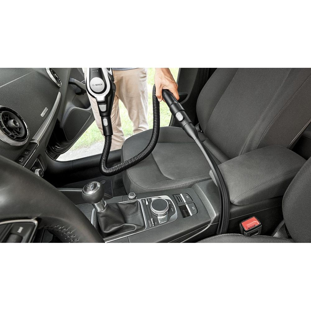 Person saugt den Autositz mit einem schwarzen Handstaubsauger und Schlauch.