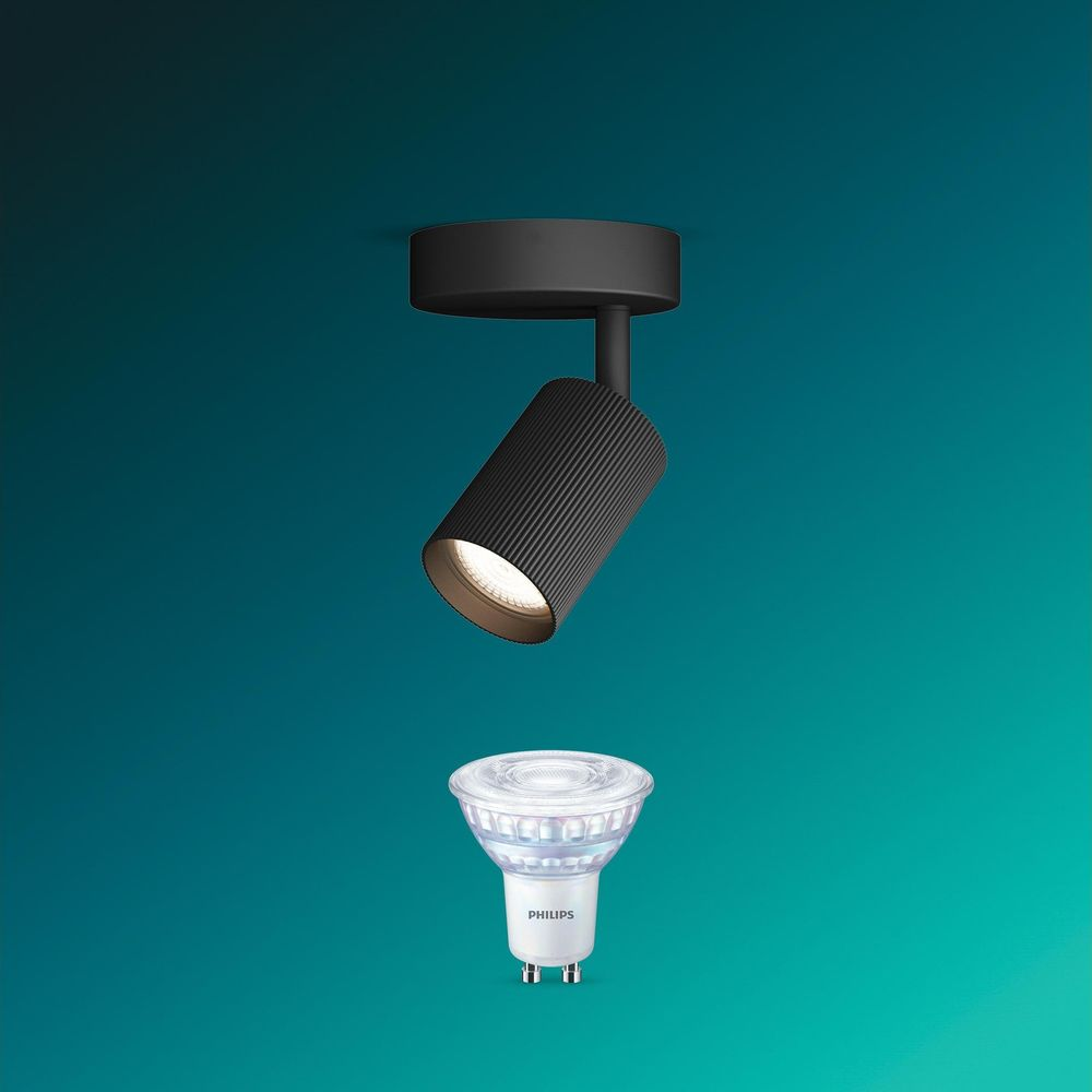 Eine schwarze Deckenleuchte strahlt Licht aus, darunter schwebt eine Philips-LED-Glühbirne vor einem türkisen Hintergrund.