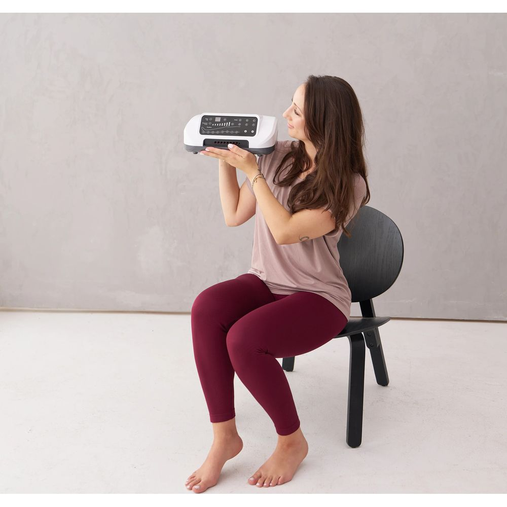 Une femme est assise sur une chaise noire, tenant une unité de commande blanche dans ses mains.