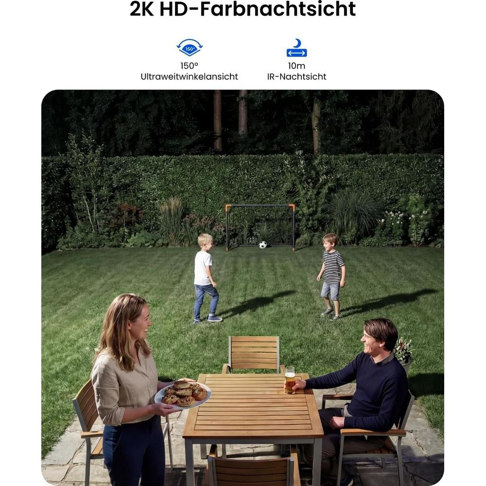 Eltern entspannen am Holztisch im Garten, während zwei Jungen Fußball spielen.