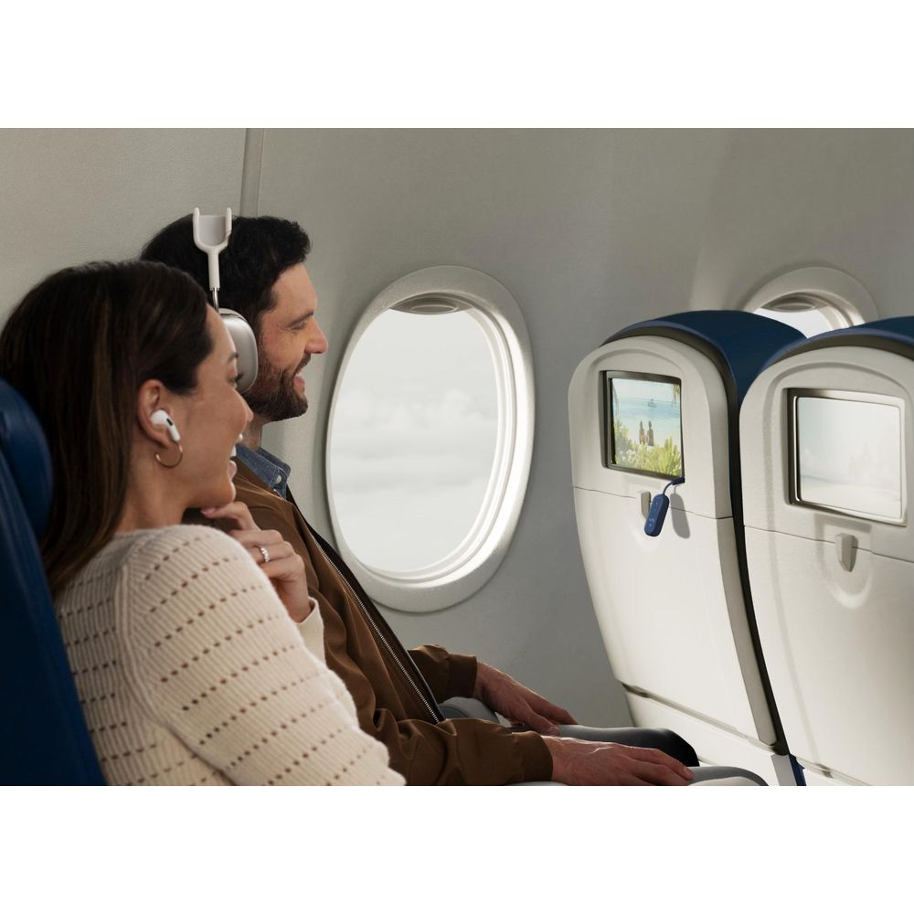 Ein Mann und eine Frau sitzen in Flugzeugsitzen, tragen kabellose Kopfhörer und schauen auf einen Bildschirm.