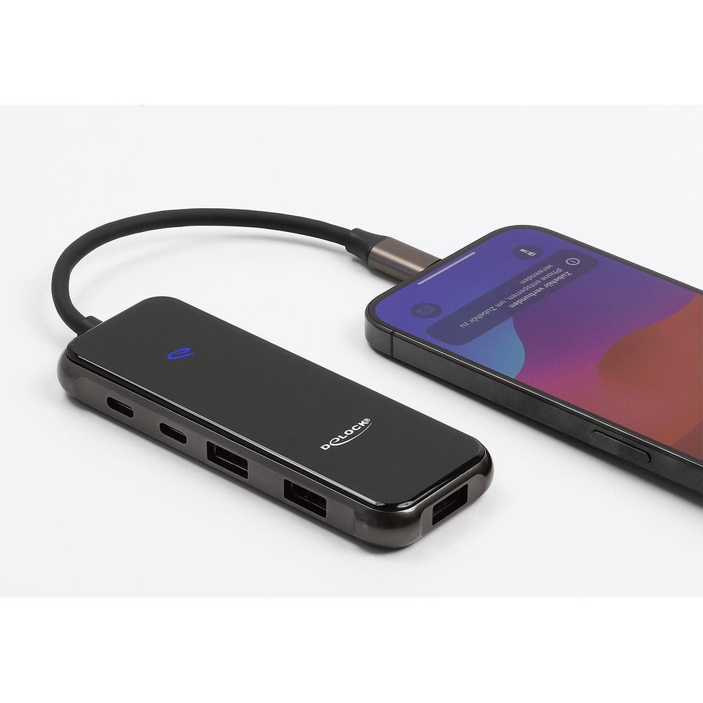 Un hub USB-C nero con più porte è collegato a uno smartphone su una superficie bianca.