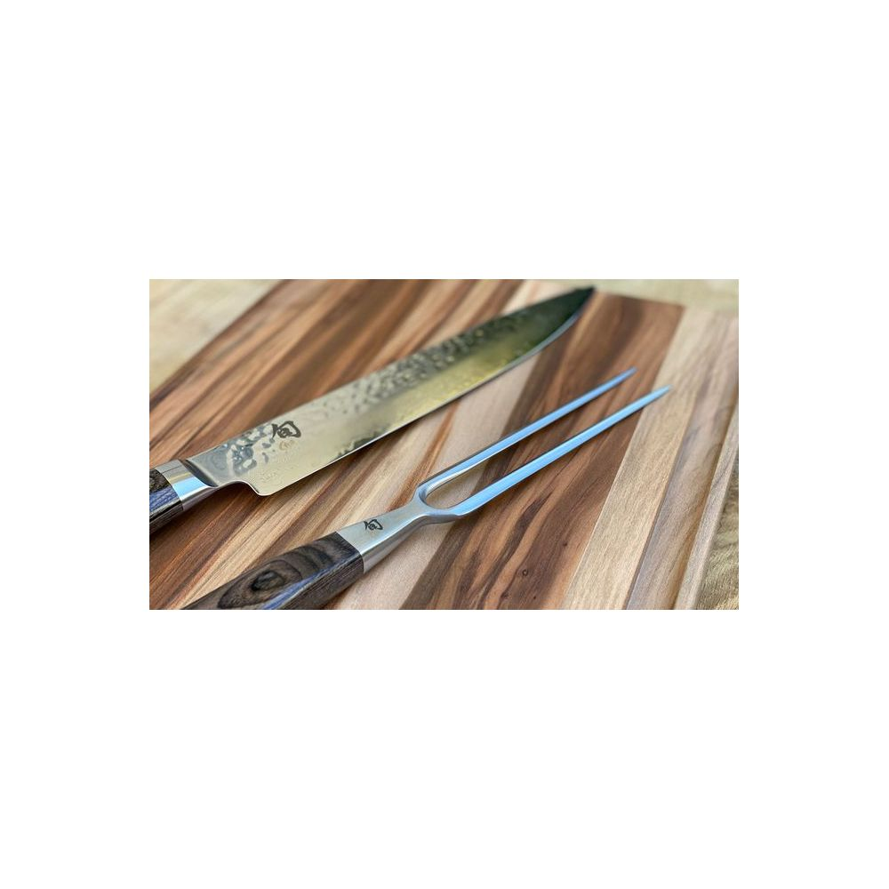 Ein großes Küchenmesser und eine Fleischgabel mit Holzgriffen liegen auf einem gestreiften Holzbrett.