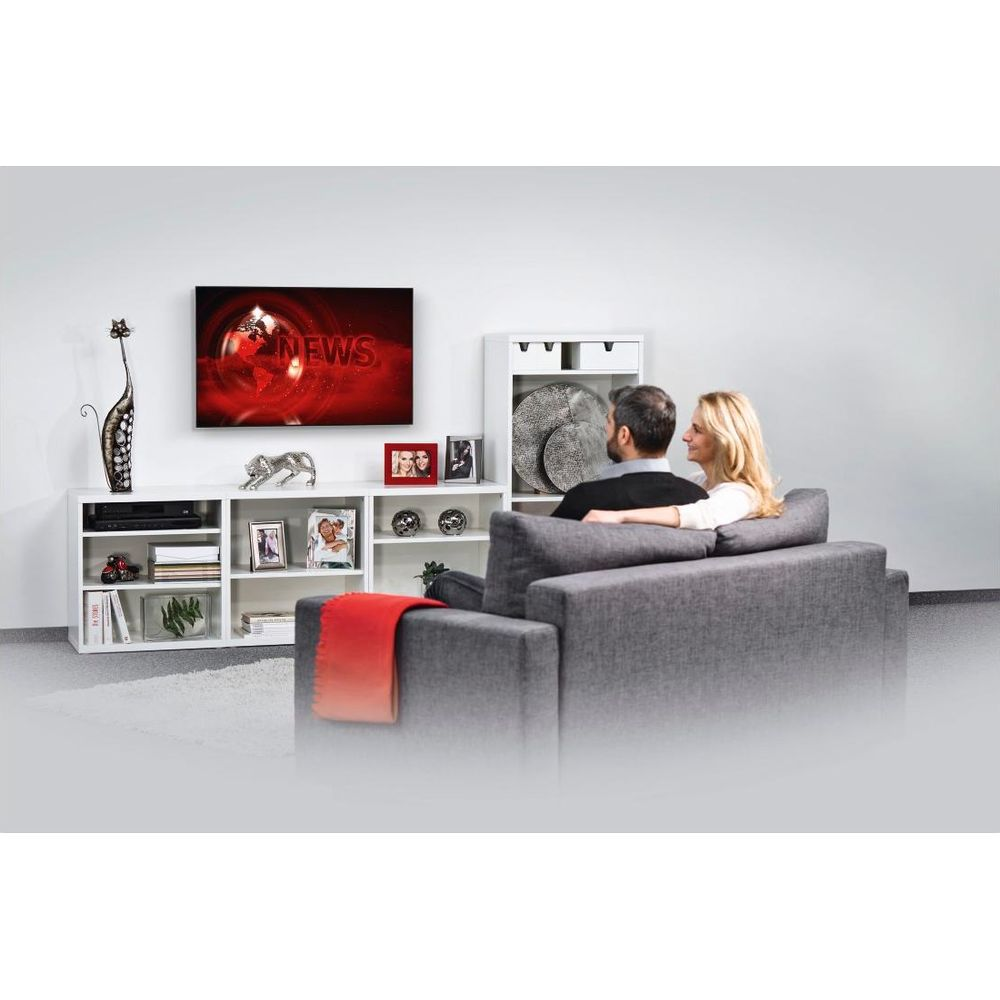 Para siedzi na szarej kanapie i ogląda TV w białym salonie z półkami i ramkami na zdjęcia.