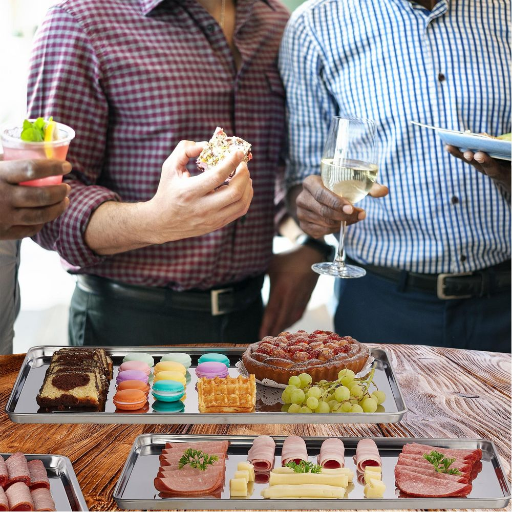 Menschen halten Snacks und Getränke bei einer Party mit Platten voller Desserts und Wurstwaren auf einem Holztisch.