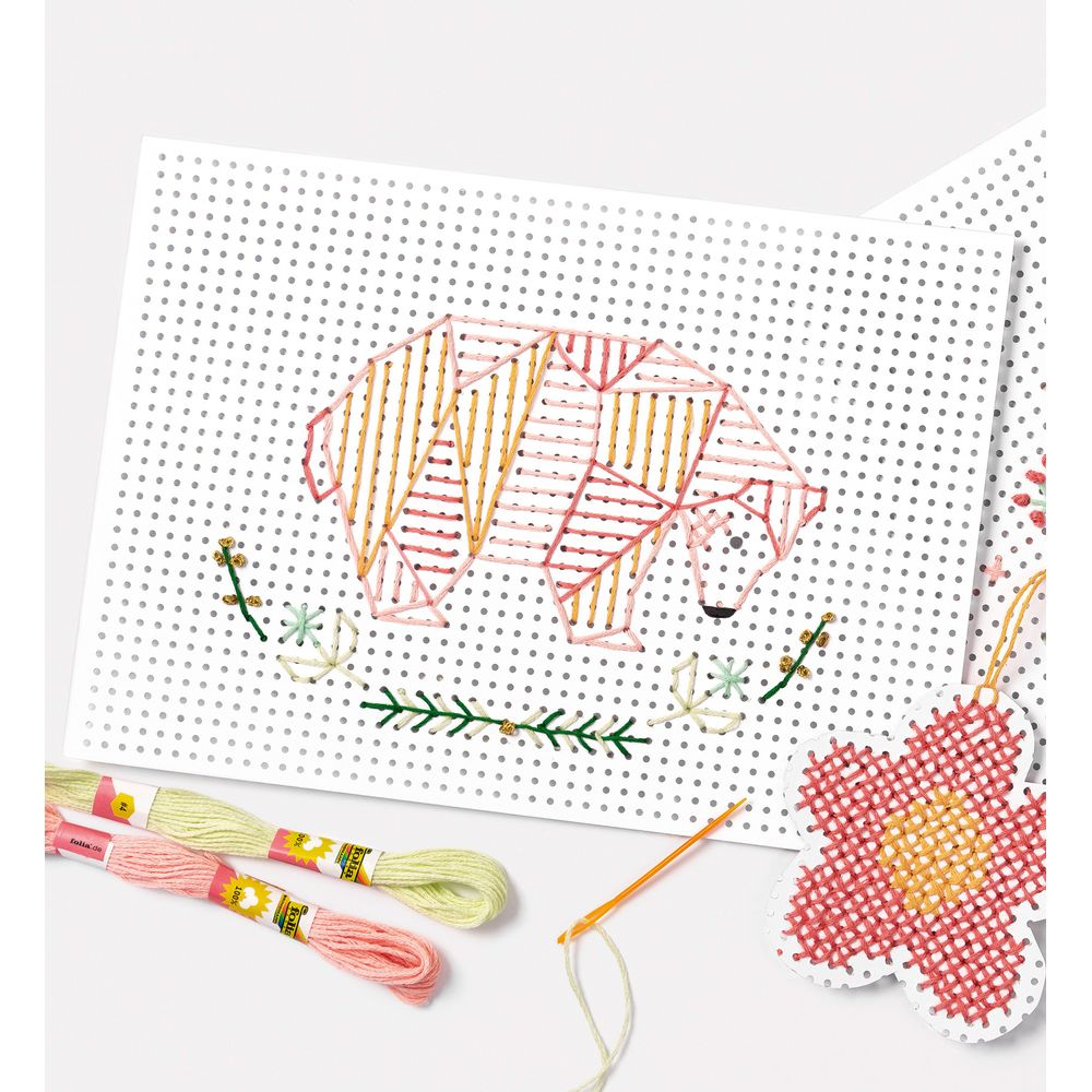 Eine Lochkarte mit rosa und gelbem Garn in geometrischer Bärenform, begleitet von Stickgarn.
