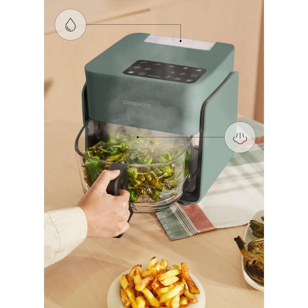 Freidora de aire verde en una mesa con patatas fritas y verduras humeantes en la cesta.
